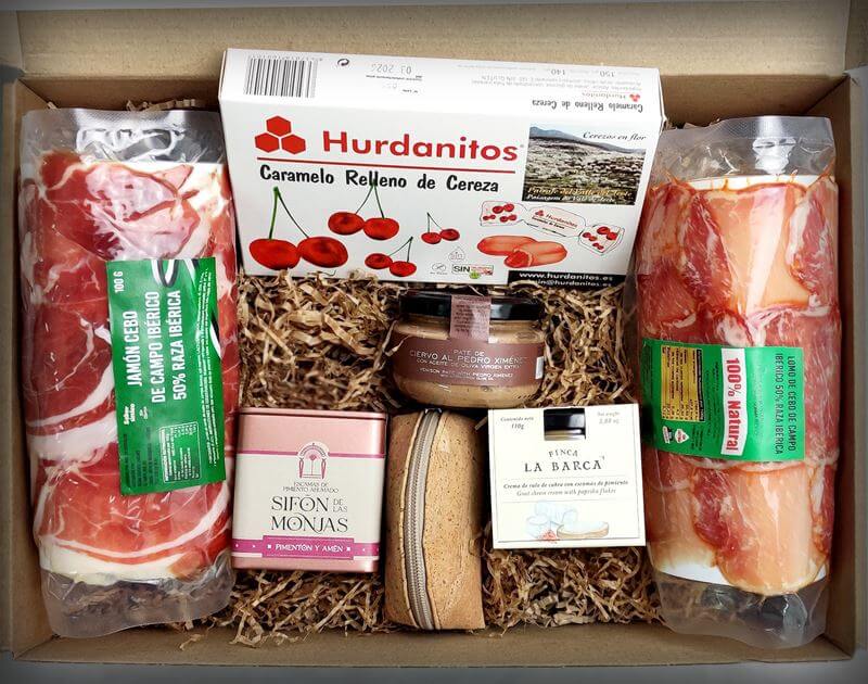 Una caja de Navidad Solidaria llena de jamón, queso y otros productos O una caja de Cestas de Navidad llena de jamón, queso y otros productos.